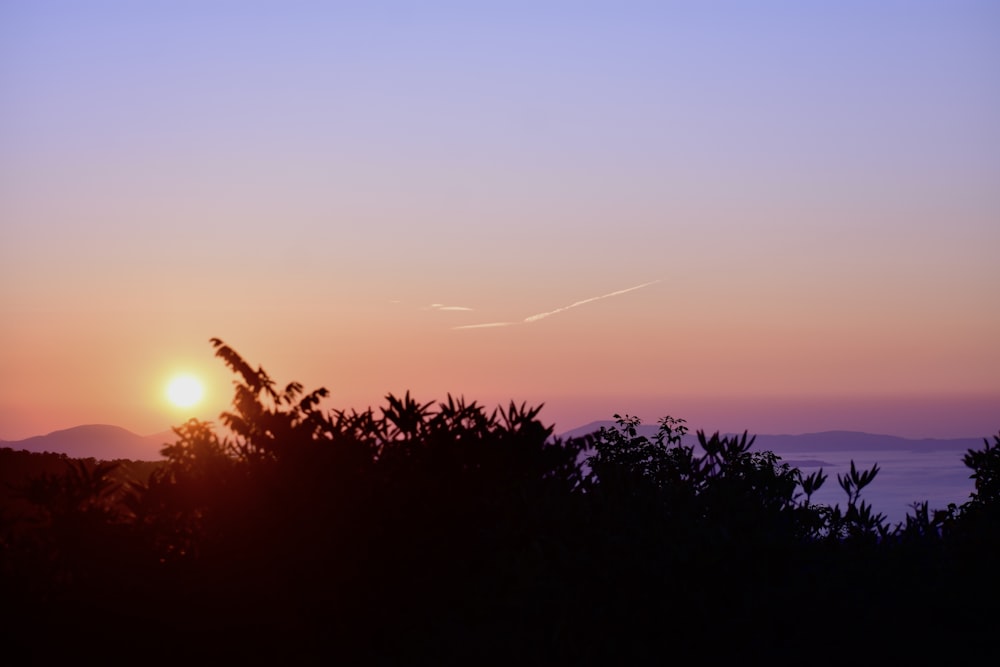 the sun is setting over the mountains and trees