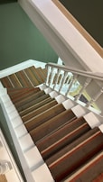A staircase with white railings and a carpet featuring green, brown, and red stripes. The walls are painted green, and the stairs ascend in a geometric pattern.