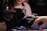A person wearing black gloves is using a nail drill on someone else's finger. The focus is on the hands and the nail treatment process, suggesting a manicure or nail care session.