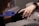 A person wearing black gloves holds another person's hand, focusing on the fingernails. The person receiving the hand treatment wears a smartwatch with a metal band.