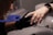 A person wearing black gloves holds another person's hand, focusing on the fingernails. The person receiving the hand treatment wears a smartwatch with a metal band.