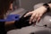 A person wearing black gloves holds another person's hand, focusing on the fingernails. The person receiving the hand treatment wears a smartwatch with a metal band.