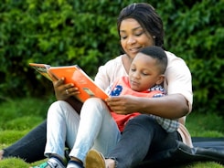 A caring teacher kneeling beside a young student, offering encouragement during reading time.