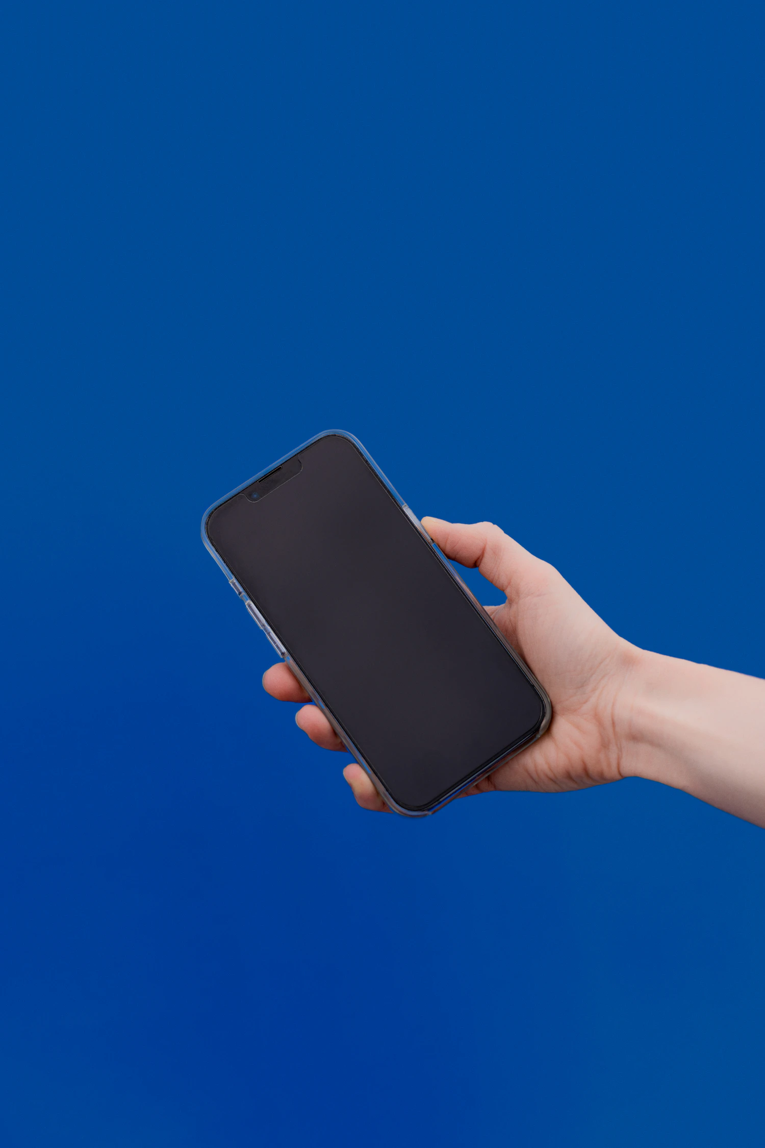 A hand holding a dark phone up against a deep blue wall