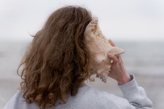 a woman with long hair holding a seashell up to her face