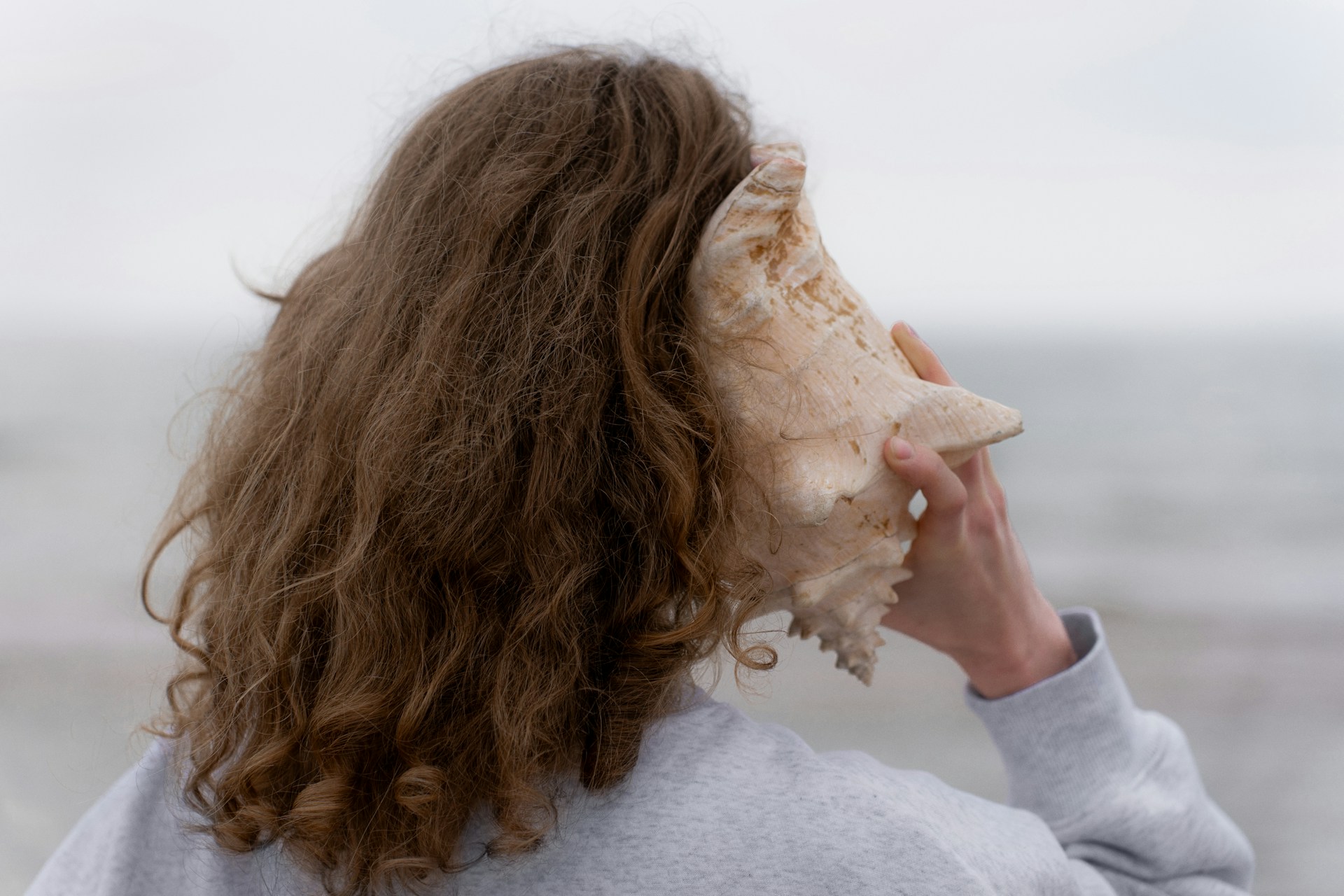 a woman with long hair holding a seashell up to her face