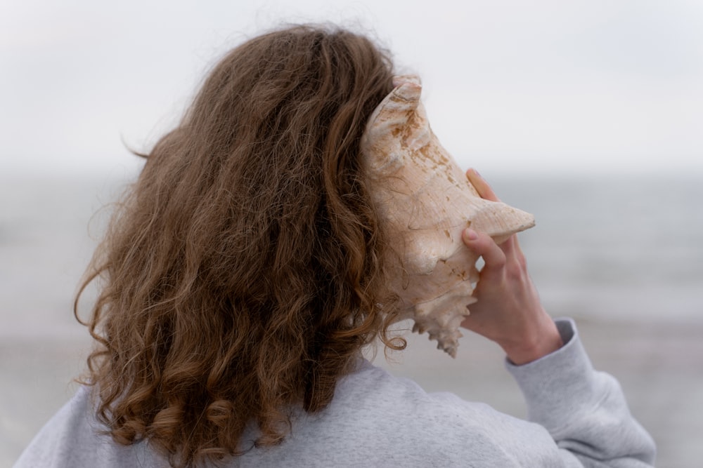 a woman with long hair holding a seashell up to her face