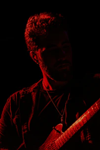 Guitarist playing an electric guitar with dramatic shadows in the background.