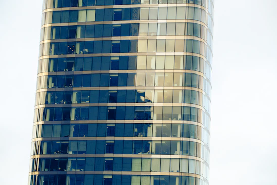 A bright, modern multi-use building with large windows showcasing apartments, office spaces, and storefronts bustling with activity.