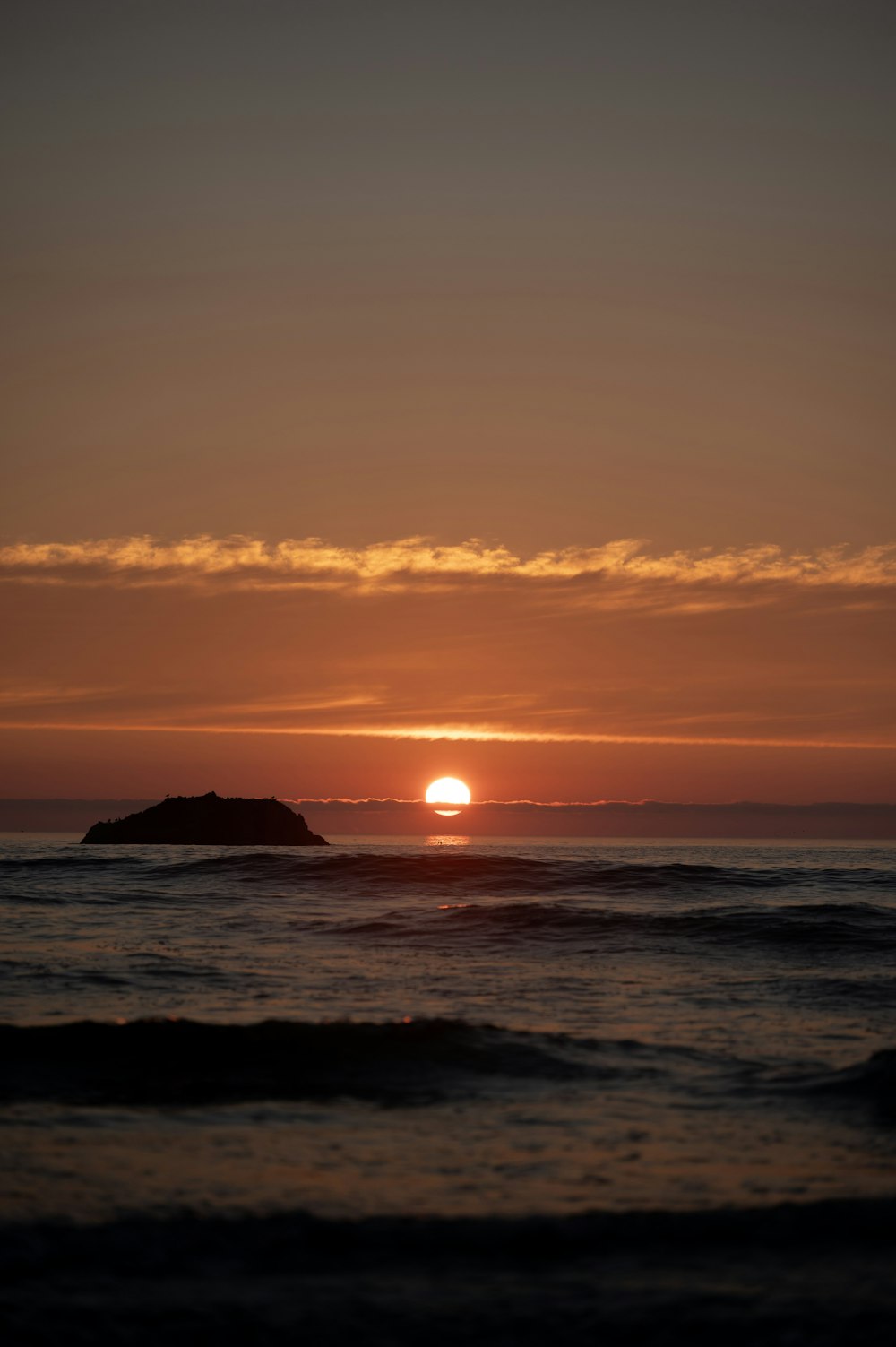 a sunset over the ocean with a small island in the distance