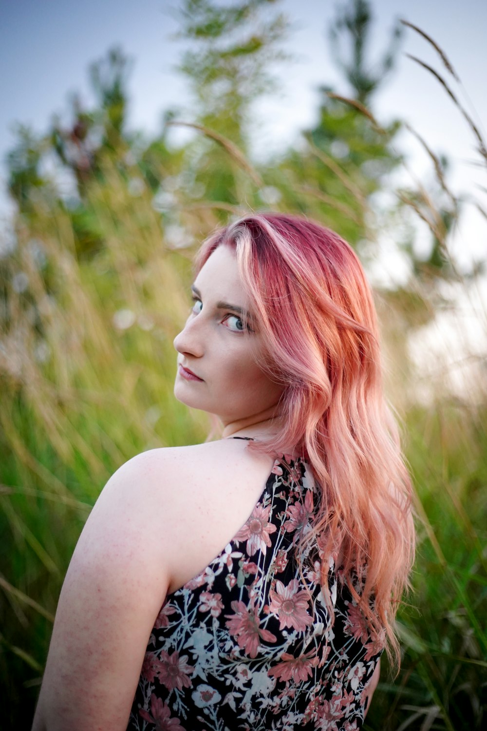a woman with pink hair standing in tall grass