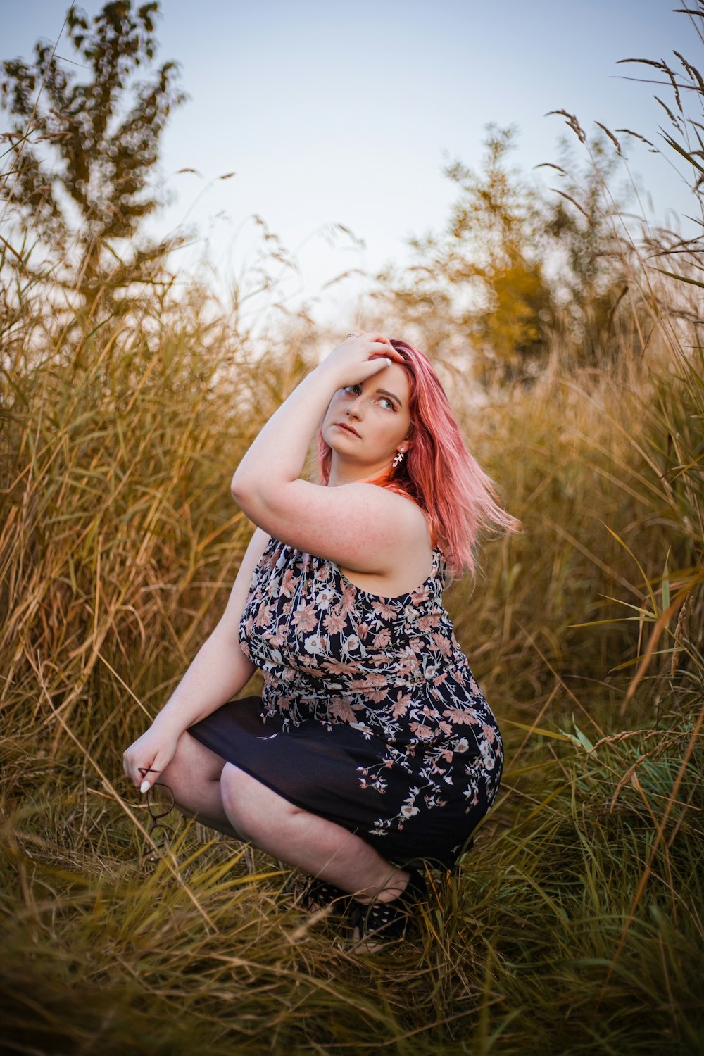 a woman with pink hair sitting in tall grass