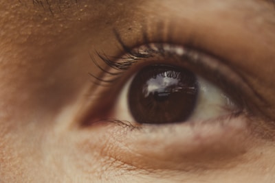 A close-up view of a human eye with detailed focus on the eyelashes and patterns around the iris, showing reflections on the eye's surface.