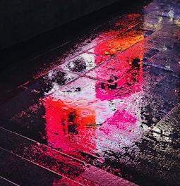 Still frame from a video showing vibrant neon signs reflecting on rain-soaked streets with blurred motion.