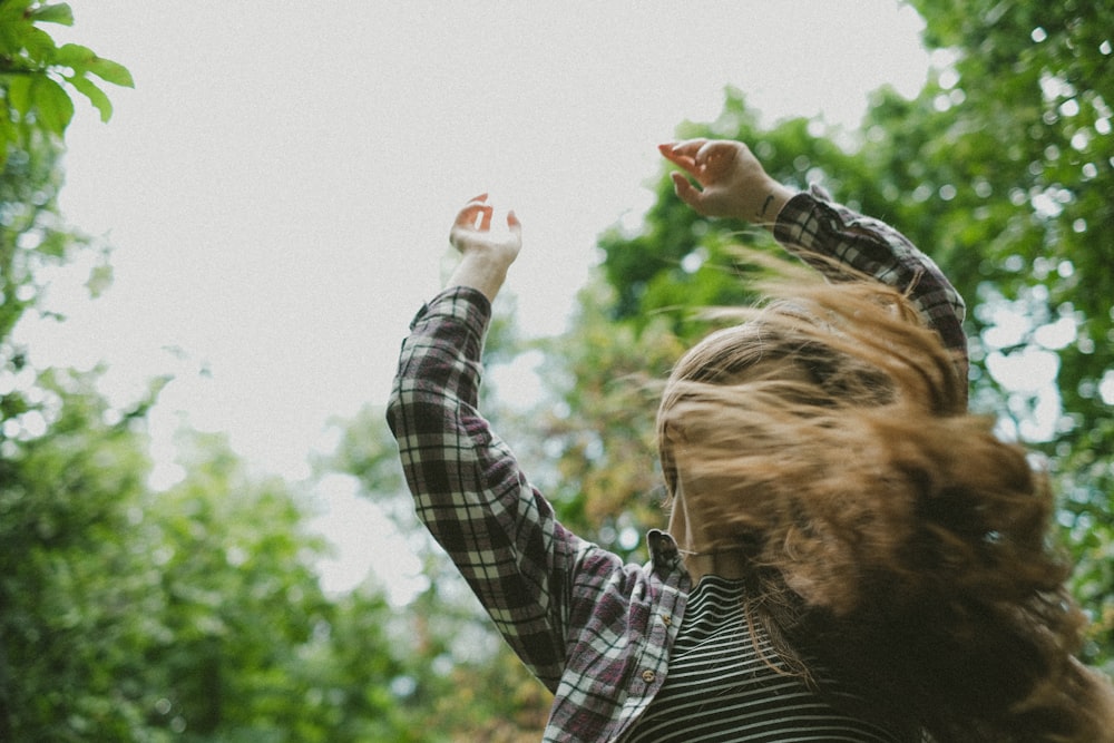 a woman in a plaid shirt reaching up into the air