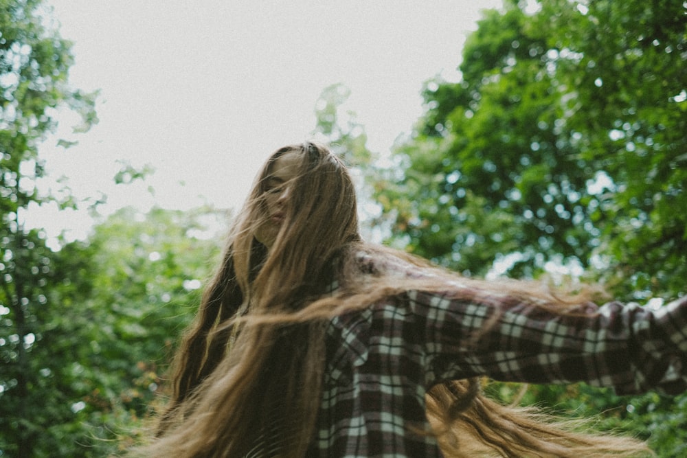 a woman with long hair walking through a forest