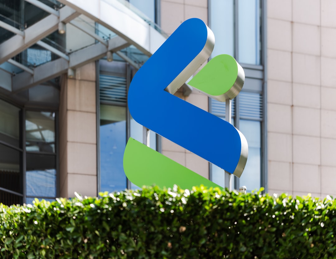 a building with a blue and green sign in front of it, Standard Chartered Bank logo placed in the grass