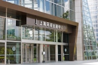 Entrance to a modern office building with large glass doors and windows, featuring the words 'Shanghai World Financial Center' in Chinese above the entrance. The reflection of surrounding skyscrapers is visible in the glass.