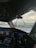 The interior of an aircraft cockpit features multiple digital displays and controls. A heads-up display is visible through the windshield, showing flight information with a view of the airport terminal and sky in the background.