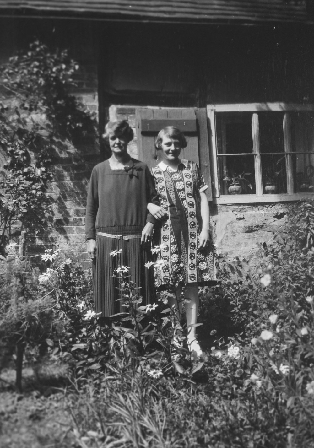 an old photo of two women standing in front of a house