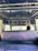 The interior of a vehicle featuring a blue, patterned ceiling with circular designs. There is a rear view of a single seat covered in a textured, purple material. A decorative item hangs from the vehicle's ceiling. The partial view of a driver's head is visible beyond the seat, with part of the road ahead visible through the windshield.