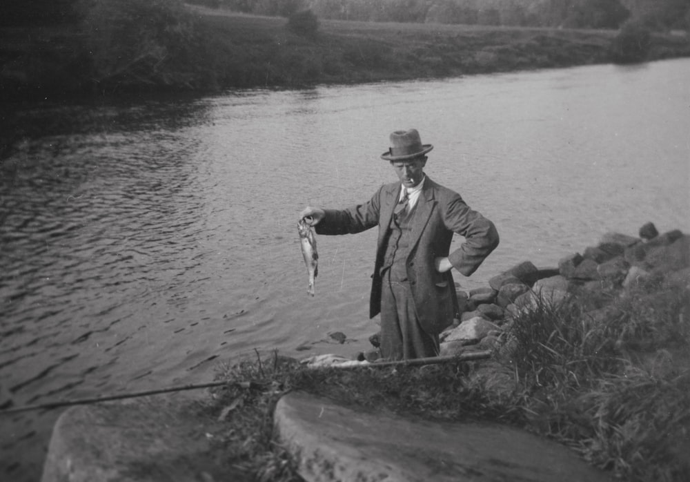 a man standing next to a river holding a fish