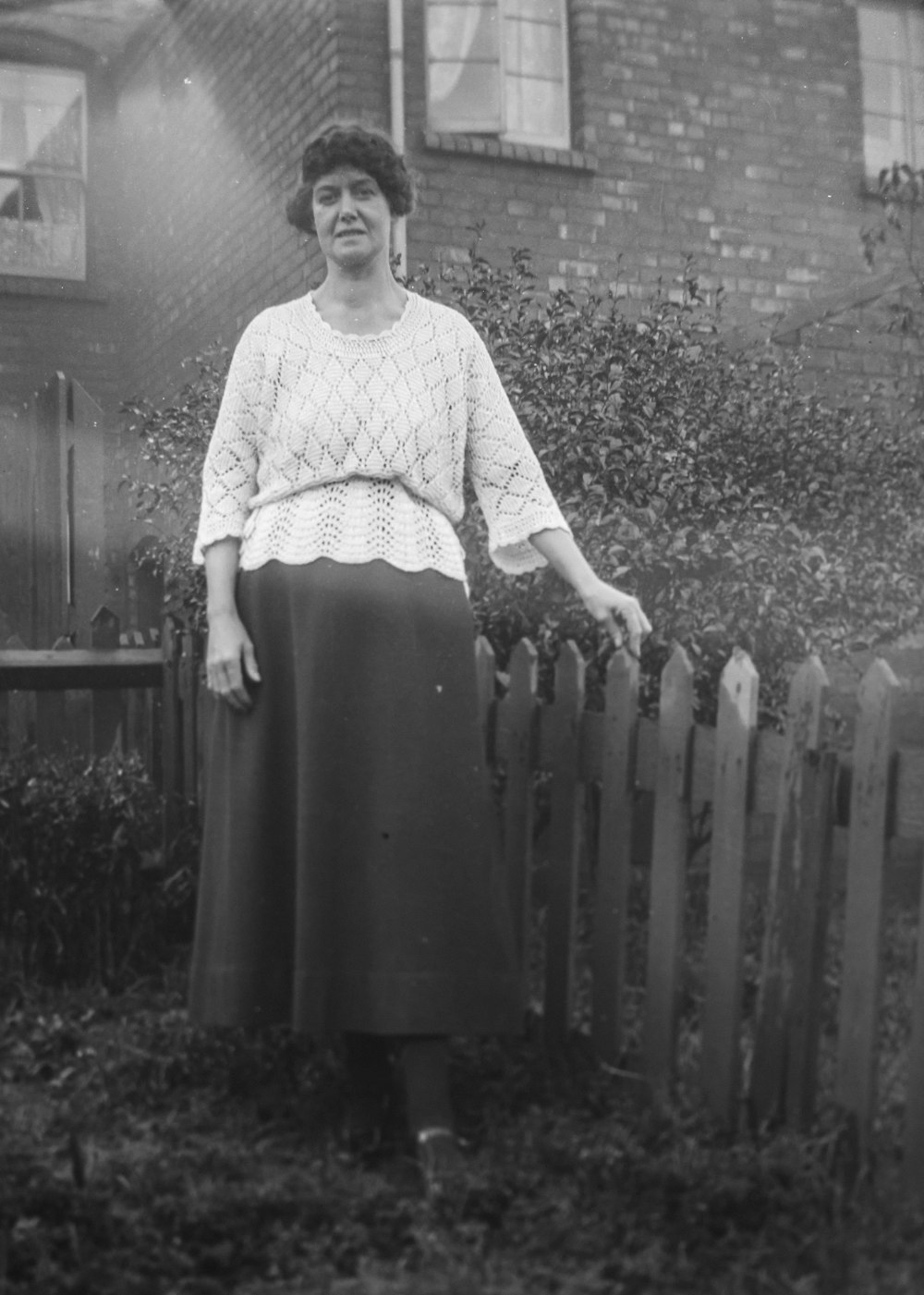 an old photo of a woman standing in front of a fence