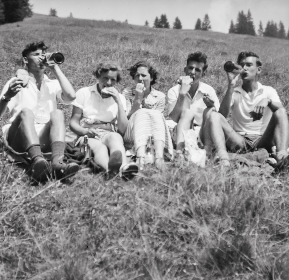 a group of people sitting on top of a grass covered field