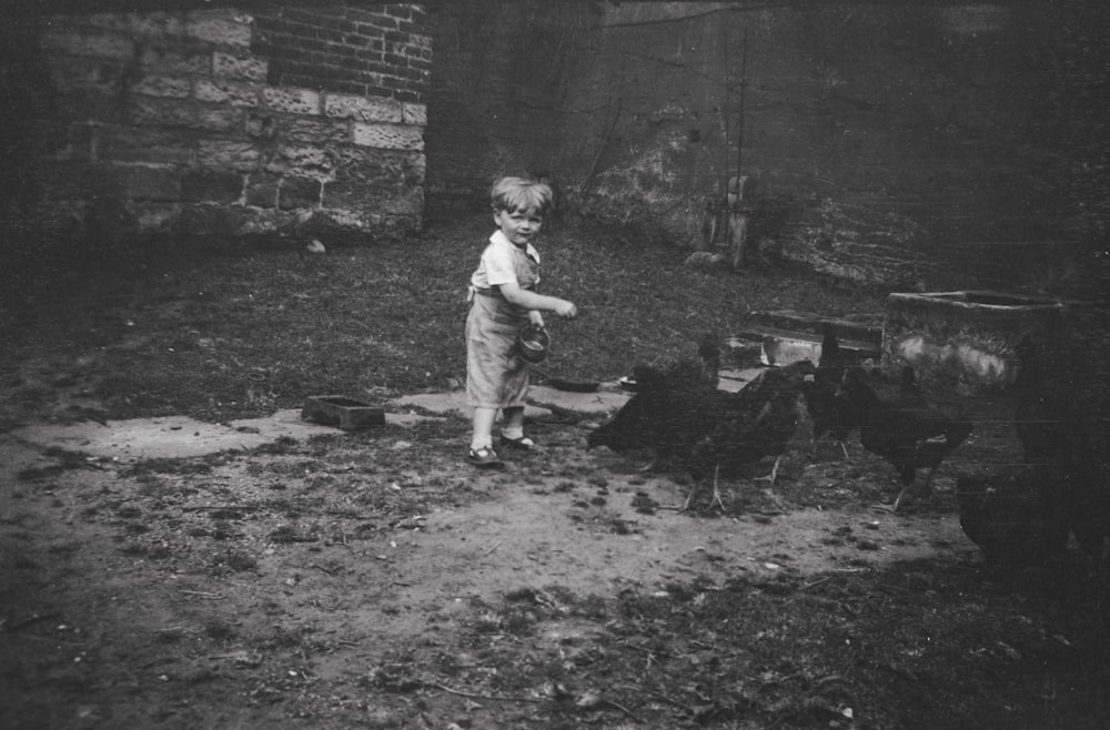 a young boy standing next to a chicken in a yard