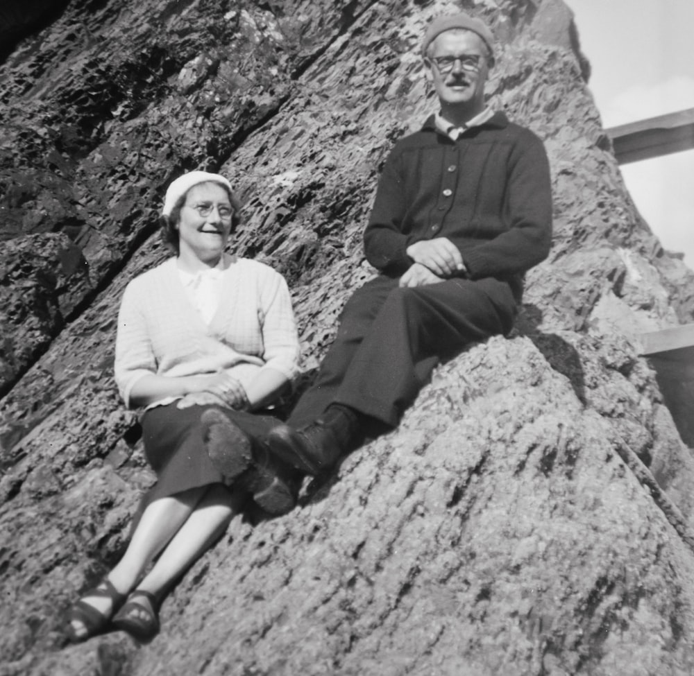 an old photo of a man and woman sitting on a rock