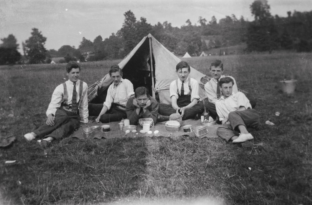 a group of men sitting on top of a grass covered field