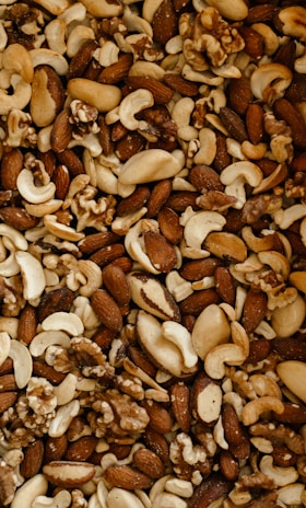 A close-up view of a variety of mixed nuts, including almonds, cashews, walnuts, and Brazil nuts. The assortment shows an appealing mixture of shapes, sizes, and textures, highlighting their natural tones and slightly oily surfaces.