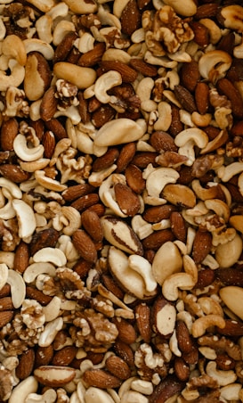 A close-up view of a variety of mixed nuts, including almonds, cashews, walnuts, and Brazil nuts. The assortment shows an appealing mixture of shapes, sizes, and textures, highlighting their natural tones and slightly oily surfaces.