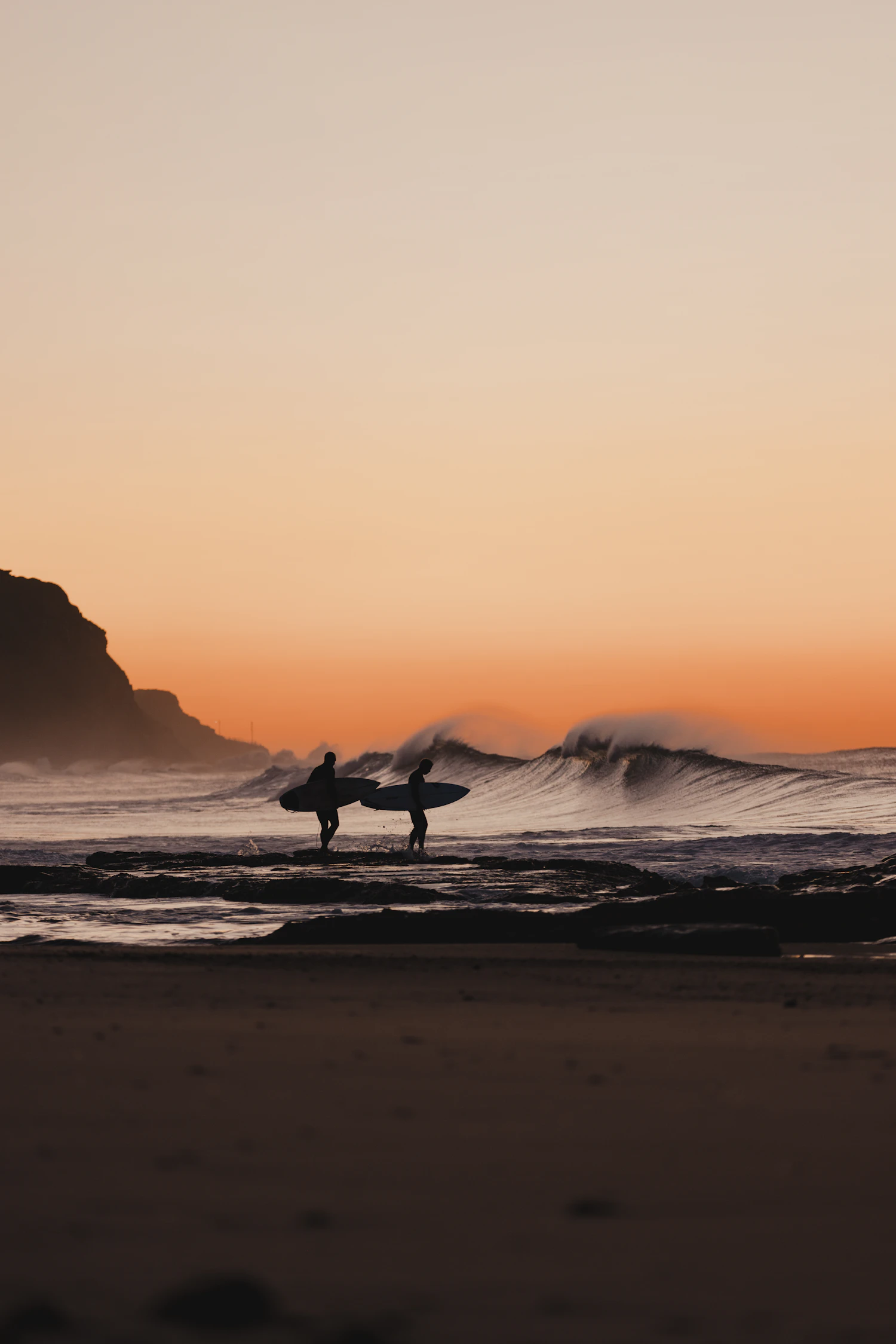 Surfer holding a surfboard on a beach at sunrise