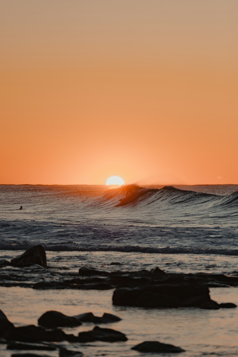 the sun is setting over the ocean with a wave coming in