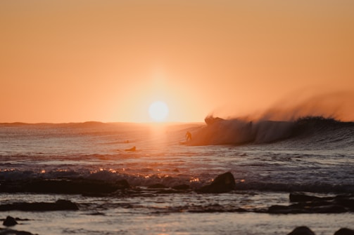 Surfer riding a powerful wave at sunset with golden light reflecting on the water.