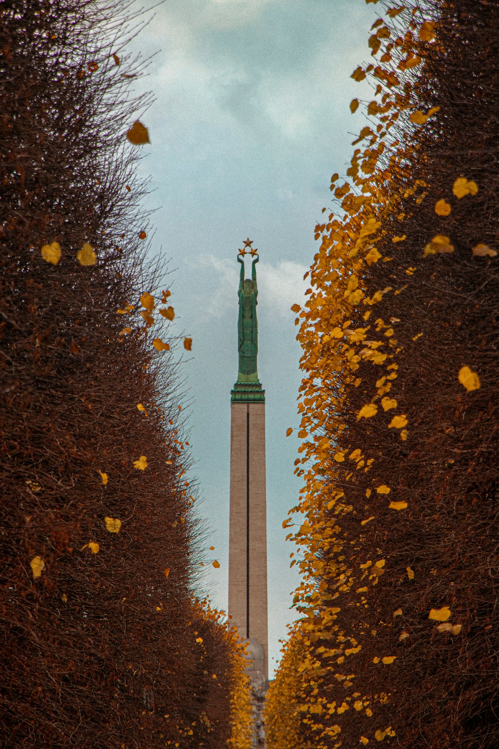 a tall tower with a statue on top of it surrounded by trees
