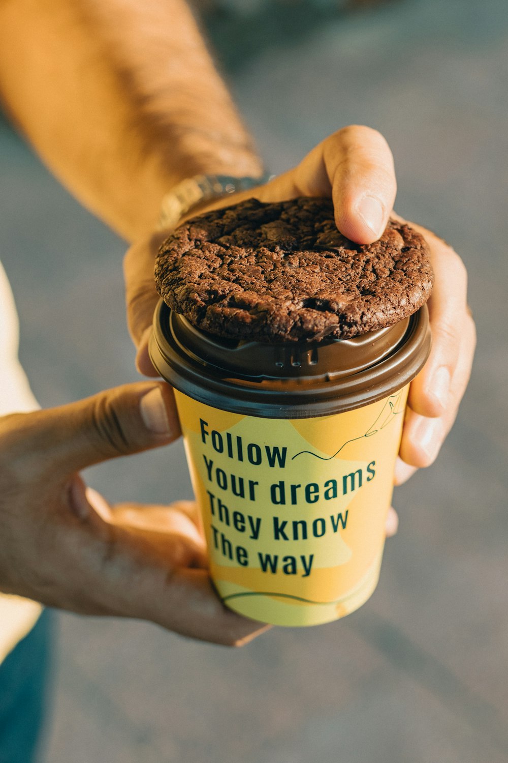 a person holding a cup of coffee with a cookie in it