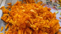 A vibrant pile of scattered orange marigold petals on a newspaper with some colorful printing visible around the edges.