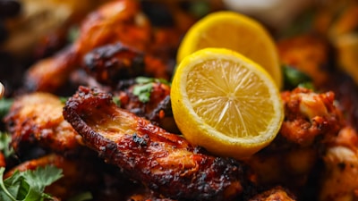 A close-up of grilled chicken wings, richly glazed and charred, garnished with two slices of lemon and sprinkled with fresh cilantro.