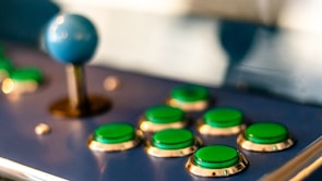 Close-up of a vintage arcade joystick with colorful buttons lit by purple lights.