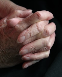 A close-up of intertwined hands against a backdrop of faded military uniforms.