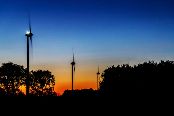Wind turbines turning gracefully on a green hillside at sunset.