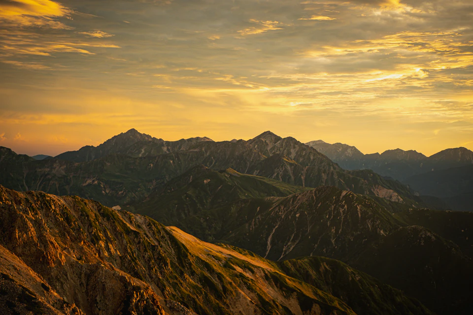 Mountain range at sunset with brown and green peaks against a golden sky