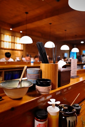 A cozy kitchen scene with neatly arranged ceramic bowls, sharp knives, and elegant chopsticks on a wooden countertop.