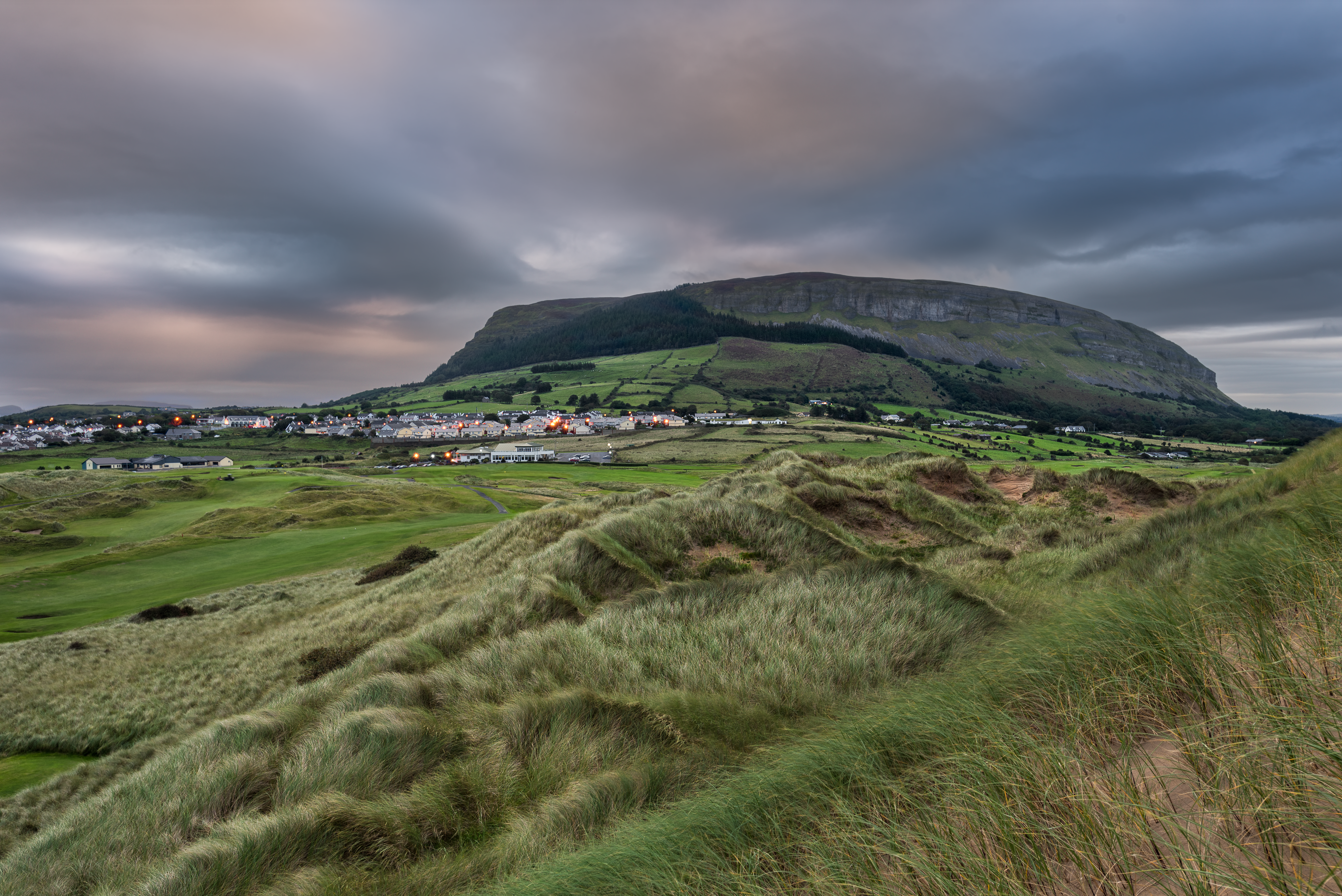 a grassy hill with a small town in the distance