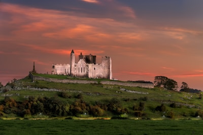 Ancient castle ruins atop a green hill under a golden sunset sky.