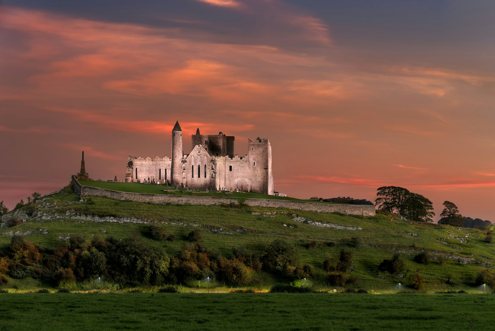 The Rock of Cashel's medieval cathedral and round tower on a green hill beneath a pink sunset sky