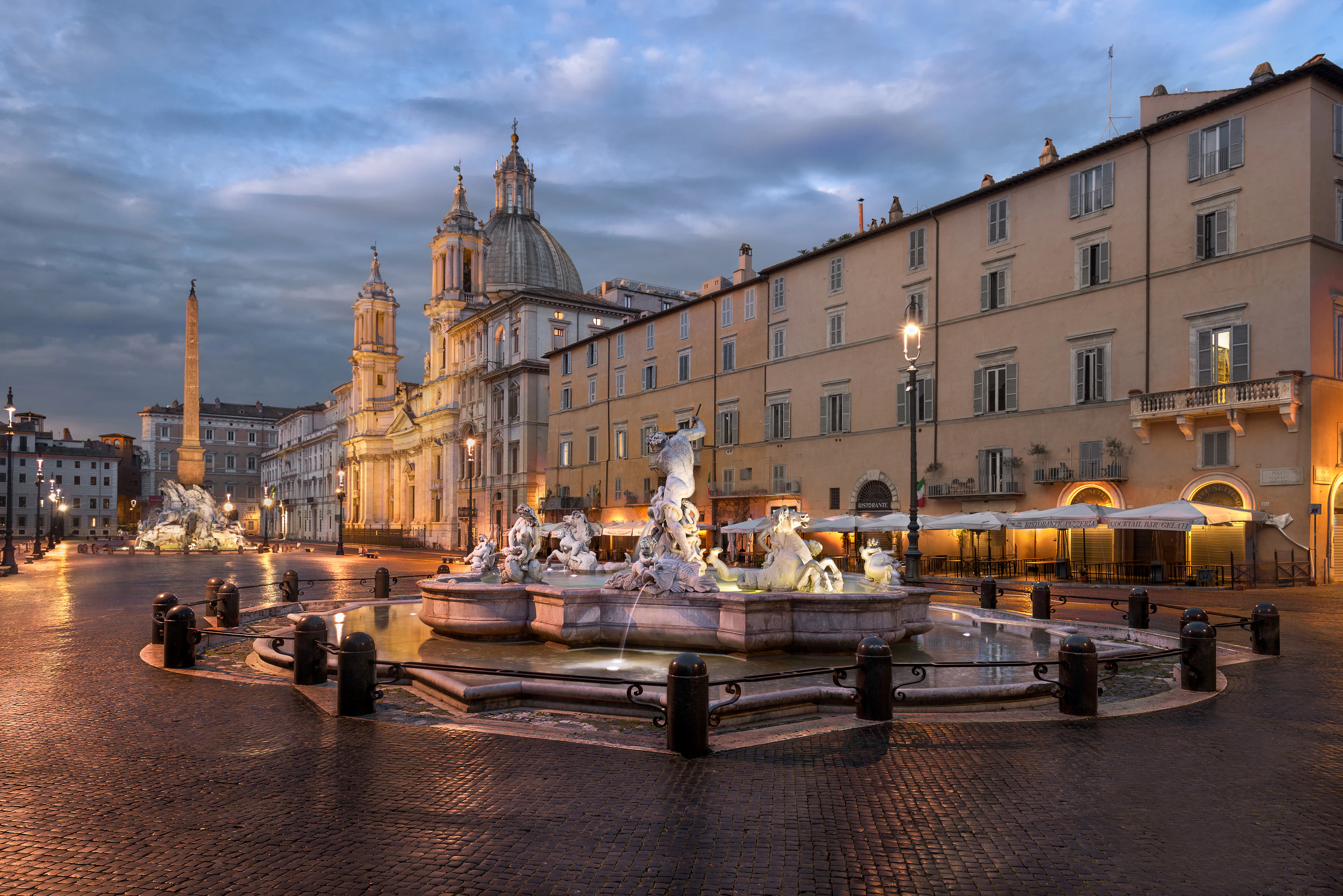 Piazza Navona at dawn: the Fountain of Neptune, the obelisk and the dome of Sant'Agnese in Agone above wet cobblestones, Rome