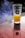 A glass with a textured surface contains a bright yellow-orange liquid resembling juice, set on a reflective surface. Smoke or mist is visible in the background, adding a dramatic effect. The glass has a label with the text 'Three Sixty Vodka.'